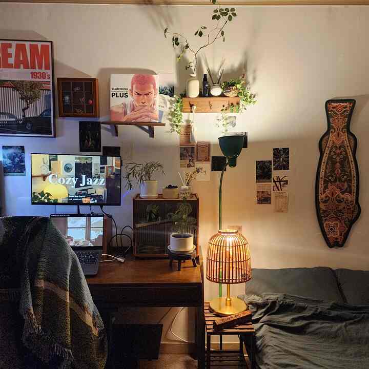 暖かい照明と植物が調和したワンルーム寝室兼書斎、木製家具と額縁がポイントの雰囲気あるインテリア
