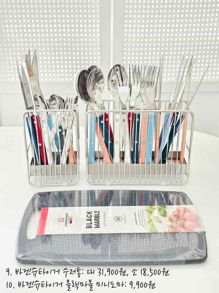 白いテーブルの上にカラフルな持ち手のステンレス製カトラリーと黒い大理石のまな板が配置されたキッチン用品のディスプレイ