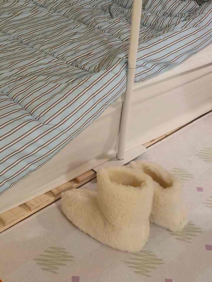 ベージュとホワイトのトーンのワンルーム寝室、ボアスリッパとストライプのベッドリネンが温かみのある雰囲気を演出しています。