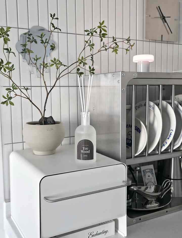Modern kitchen with white tiled walls and stainless steel rack, featuring a plant in a pot and a diffuser on a white appliance, creating a clean atmosphere