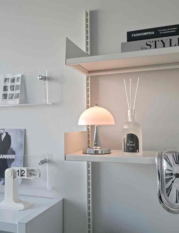 A clean, simple space with white and silver tones featuring mid-century modern wall shelves and a table lamp