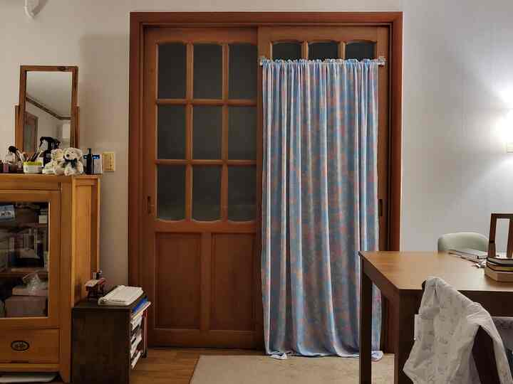 木目調とベージュが調和するワンルームのリビング兼ダイニング空間、木製家具と花柄カーテンがヴィンテージな雰囲気を演出しています。