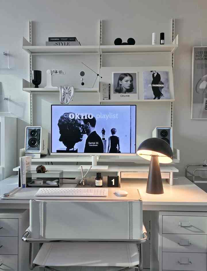 Modern white-toned home office featuring a clean desk, office chair, monitor, and table lamp creating a practical workspace
