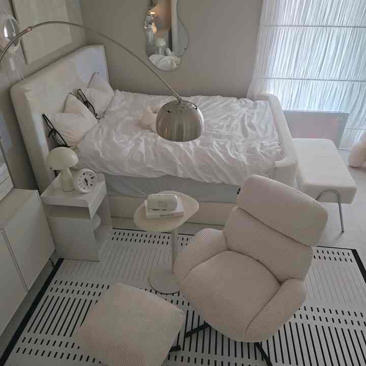 白を基調とした寝室、モダンでミニマルな家具配置とシルバーのフロアランプが印象的な居心地の良いインテリア