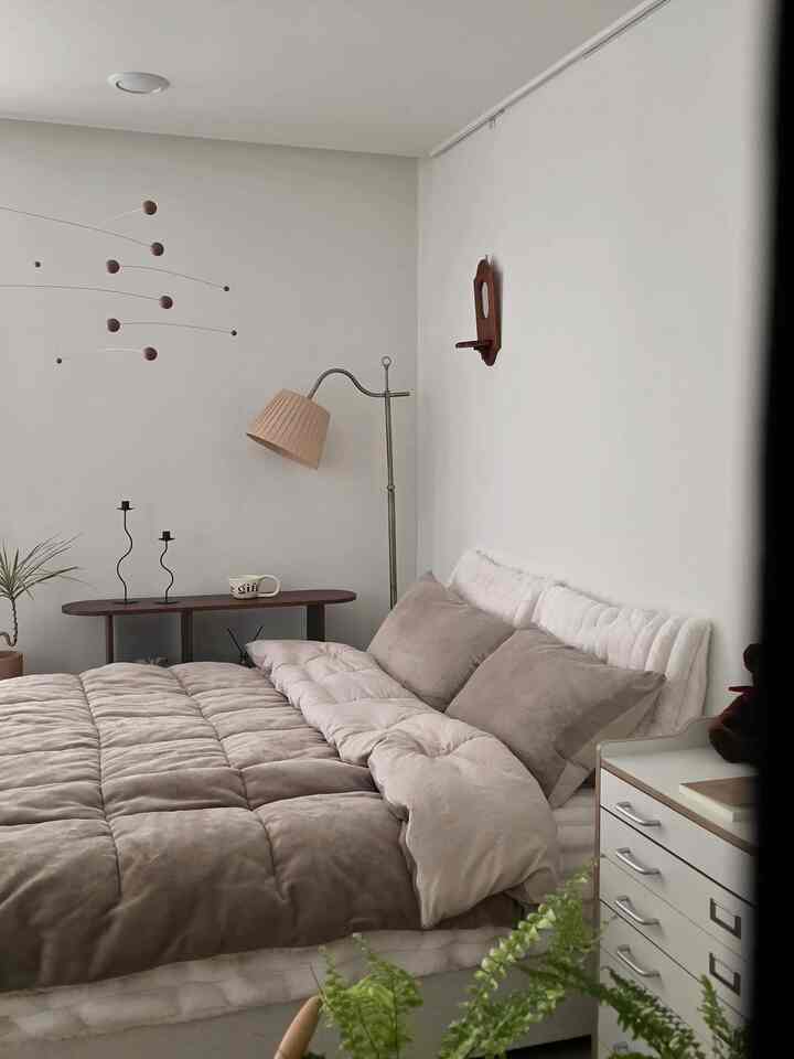 明るい木目調と白色が調和した寝室、クイーンサイズベッド、フロアランプ、モビールが配置されたナチュラルモダンなインテリア