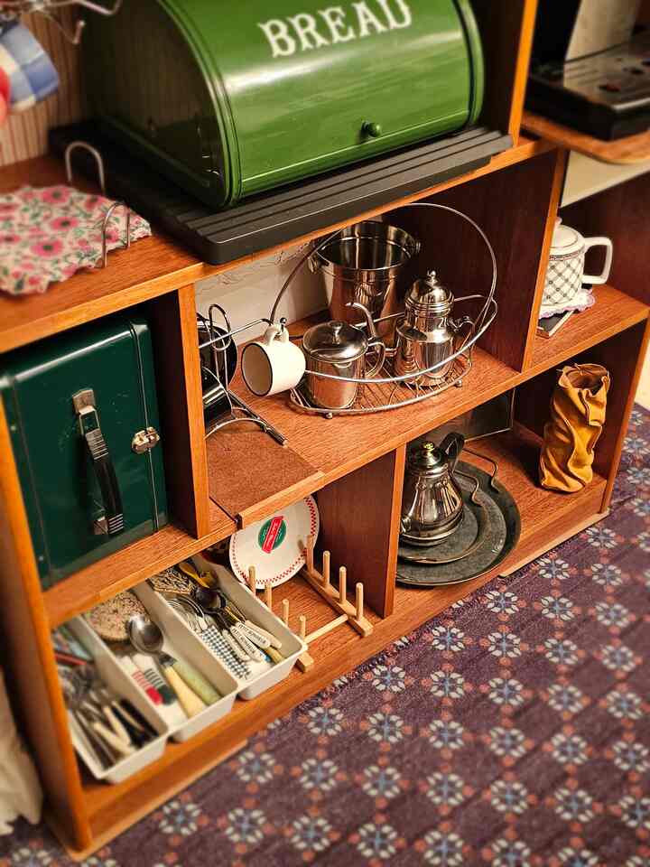 温かみのある木目調の本棚にヴィンテージのキッチン用品が配置されたおうちカフェ、紫色の柄付きラグが敷かれた印象的な空間