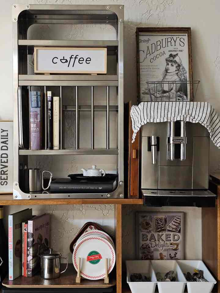 木製の棚とステンレスのキッチンラック、コーヒーマシン、ヴィンテージの額が配置された暖かく雰囲気のあるキッチン