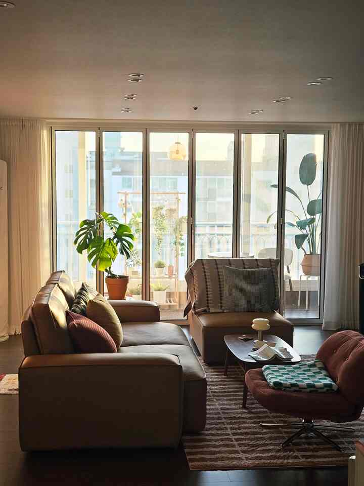 Warm brown-toned living room featuring a large glass window, spacious sofa, and greenery for a natural ambiance