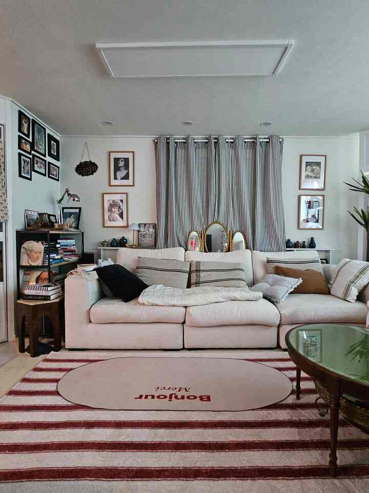 ホワイトとウッドトーンが調和するヴィンテージスタイルのリビングルーム、クリーム色の4人掛けソファと赤のストライプラグが配置されたフレンチカントリームードのインテリア