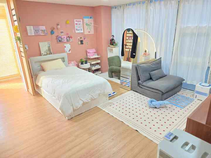 ピンク色の壁と白いベッド、グレーのソファが配置された子供部屋のような寝室空間