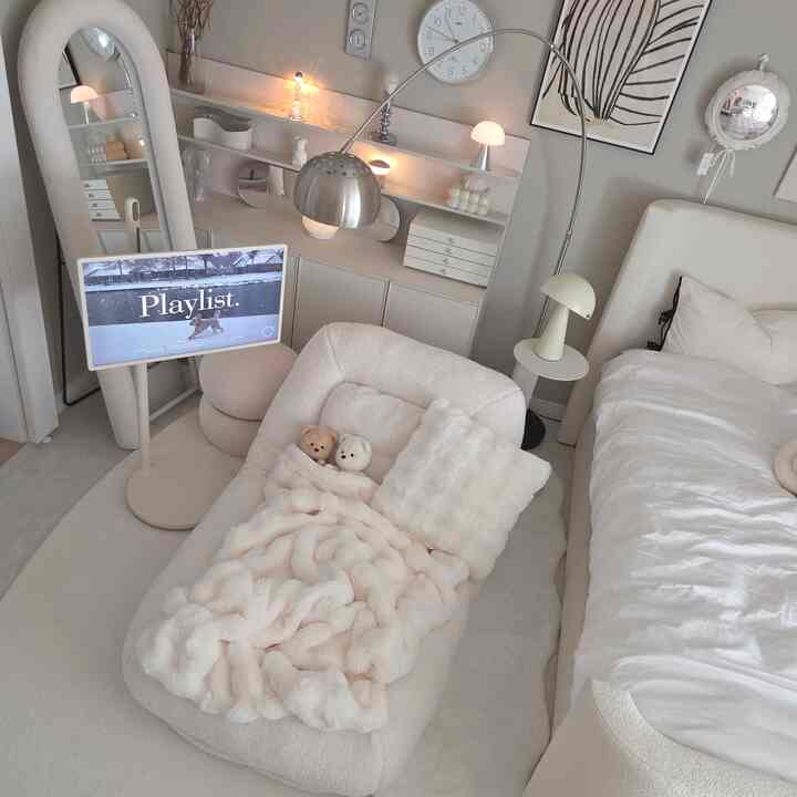 アイボリーとホワイトのトーンが特徴的なワンルーム寝室、中央に角度調整可能なフロアファブリックソファが配置され、右にベッドがある落ち着いた雰囲気の空間