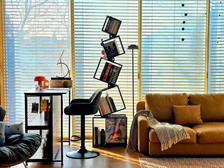 Wood-toned living room with prominent blinds, featuring a modern sofa and unique bookshelf in a cozy home office setting