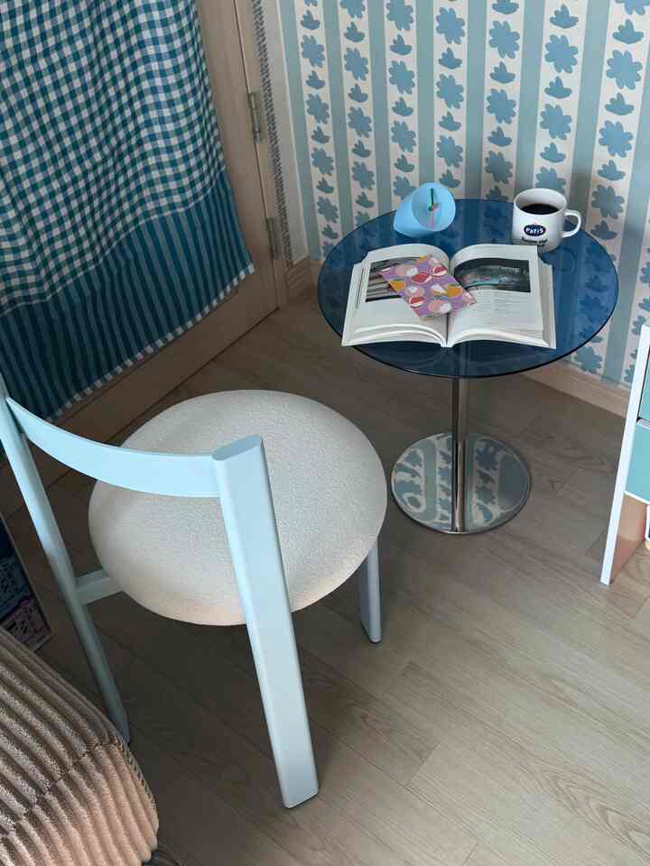 A cozy home cafe space in pastel blue and white tones featuring a round blue table and light blue dining chair in a small room