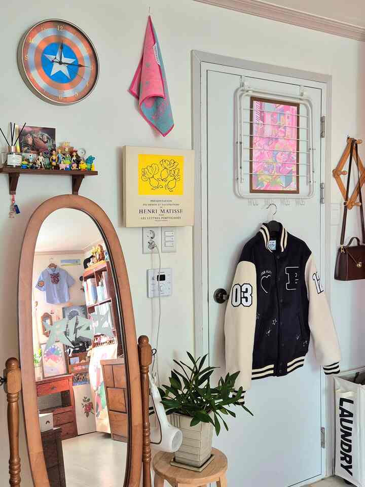 White-walled studio apartment featuring a wooden full-length mirror and wall shelf with toys, creating a cozy atmosphere