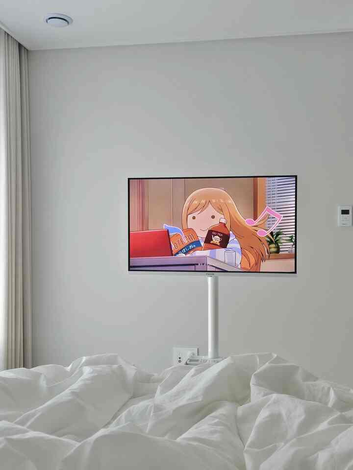 ホワイトトーンが支配的なミニマルな寝室、清潔感のある白い寝具と中央に設置されたスタンド型テレビが配置された落ち着いた空間