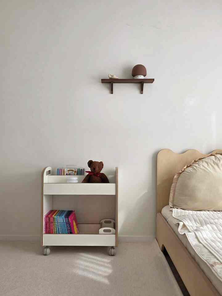 白とベージュの色調の子供部屋、木目調のベッドとおもちゃの収納カートが配置された落ち着いたインテリア