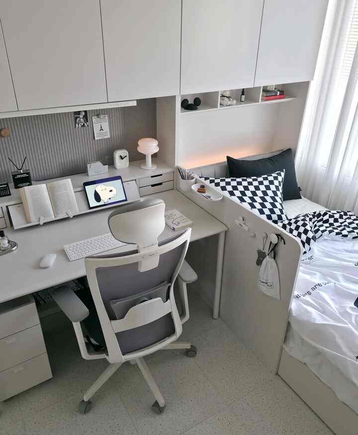 ホワイトとグレーの色調の寝室兼ホームオフィス、シンプルでモダンな空間にデスクとオフィスチェアが配置されている