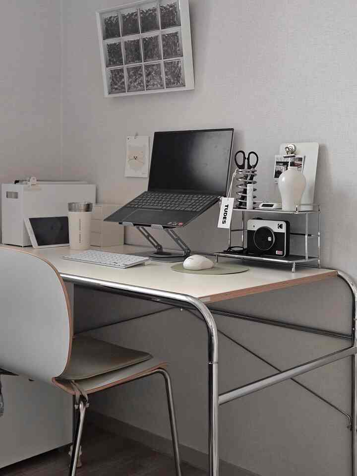White and chrome compact home office space featuring a simple desk with laptop on a monitor stand, creating a clean and minimal work environment