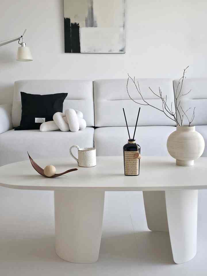 明るい白とモノトーンのリビング、モダンなソファとコーヒーテーブルにディフューザーとナチュラルなオブジェが配置されたシンプルなインテリア