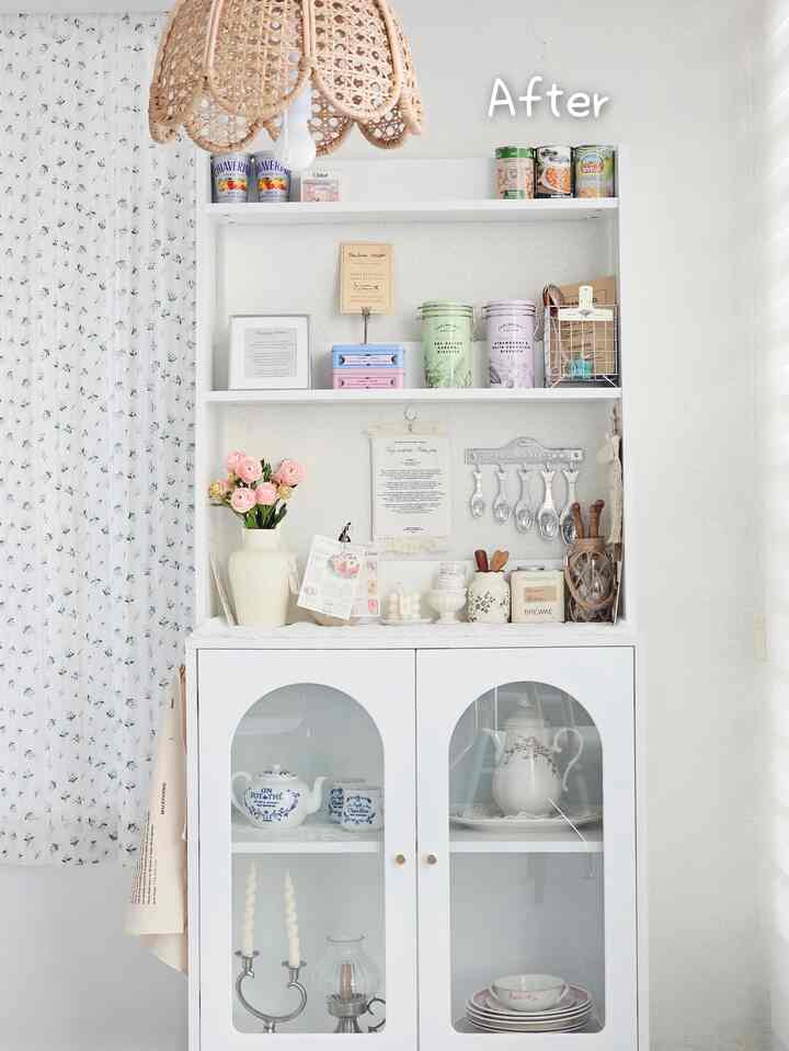 白を基調としたキッチンスペース、ヴィンテージ風のティーポットや食器が並ぶ収納キャビネットが配置された雰囲気のあるインテリア