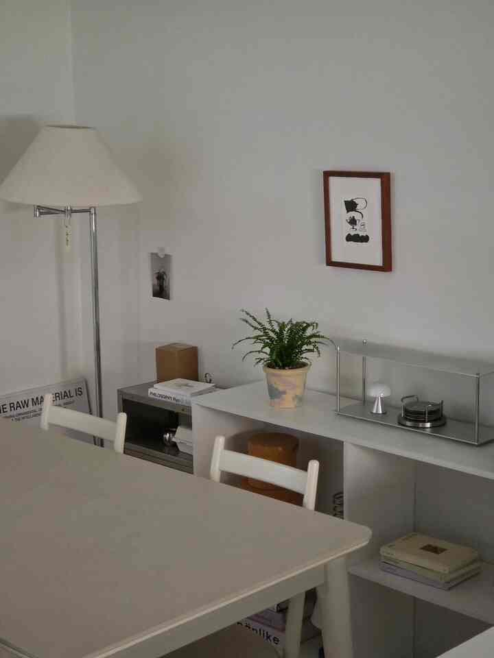 白とベージュの色調のミニマルなダイニング、ダイニングテーブルと椅子、フロアランプ、棚の上の植物が配置された落ち着いた空間