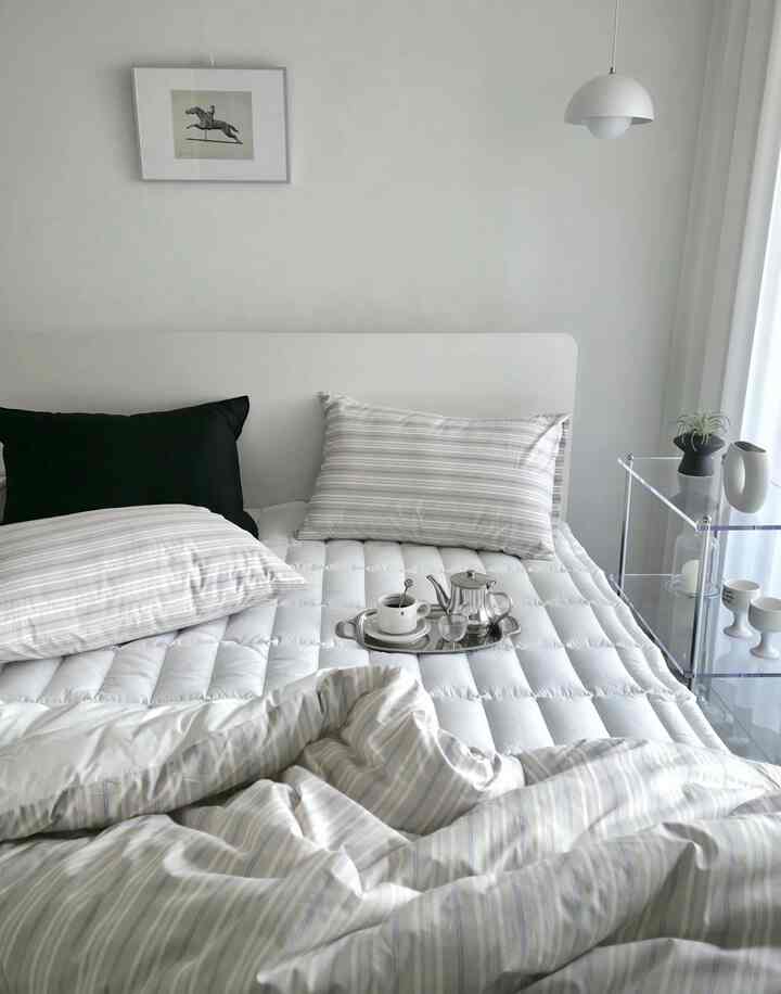 White and gray toned bedroom featuring a clean bed with striped pillows and pendant light in a minimalist modern space