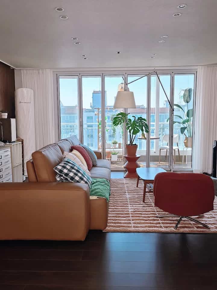 ナチュラルカラーとブラウン調のリビング、大きな窓、レザーソファ、フロアランプが配置された温かみのあるインテリア