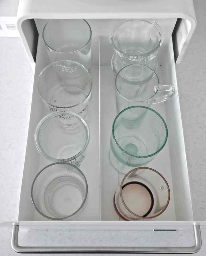 ホワイトトーンのキッチンキャビネットの引き出しにさまざまな透明なカップが整然と並ぶ清潔感のある空間