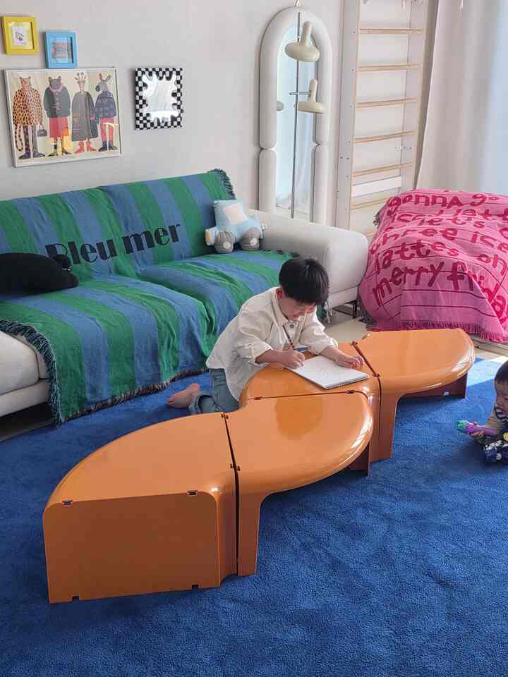 ブルーとオレンジが印象的なリビング空間、子供が学習するテーブルとソファが配置されたモダンなインテリア