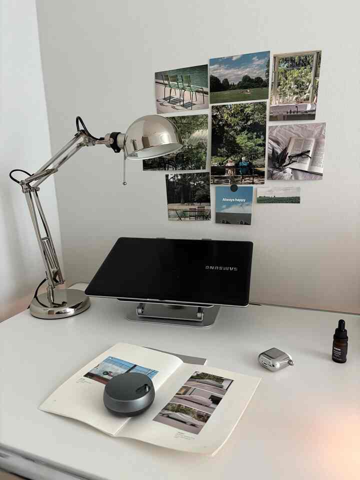 白を基調としたコンパクトなホームオフィスのデスク、シルバーのランプとノートパソコンスタンドが配置された清潔感のある作業空間