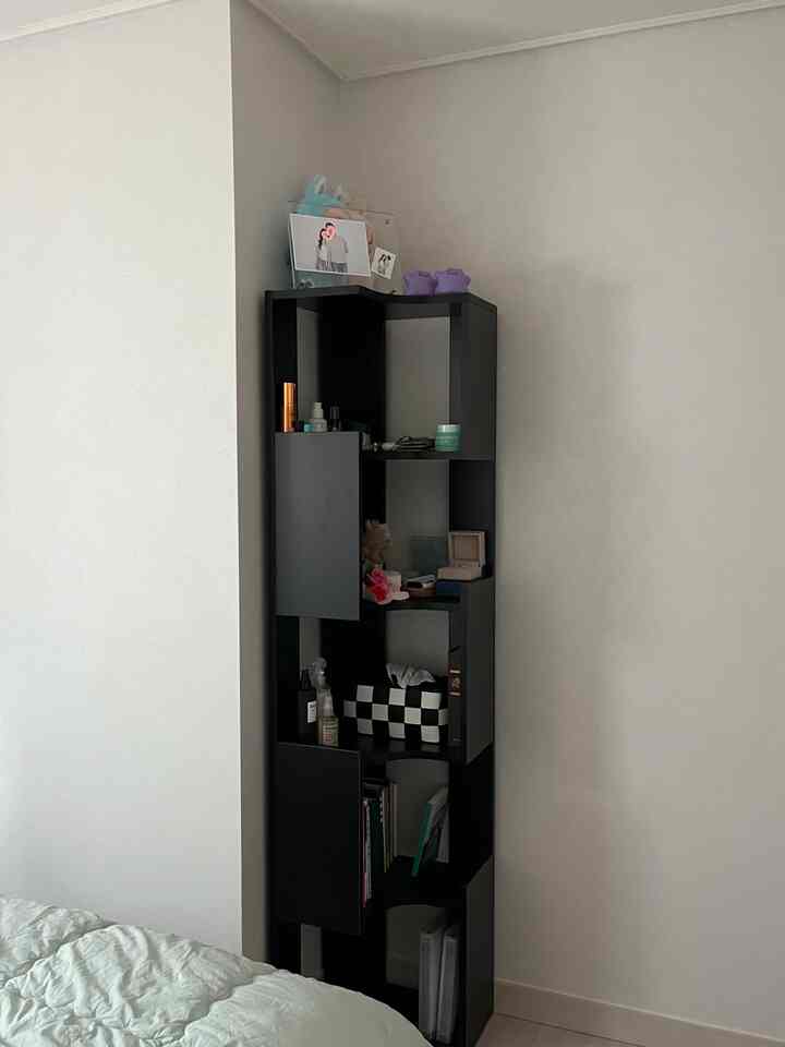 白い壁と黒のコーナー収納が配置されたモダンな小さな寝室、落ち着いた雰囲気のベッドが見える