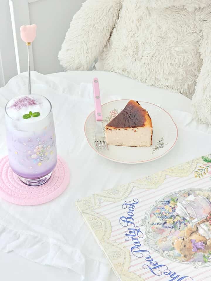 ホワイトとピンクのトーンのカフェ風空間、ケーキとラベンダードリンクが配置された雰囲気あるテーブル