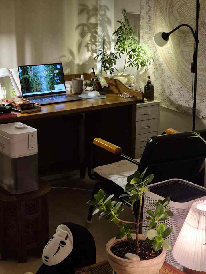 暖かい照明のヴィンテージアームチェア、デスク、多様な植物が配置されたワンルームの作業スペース