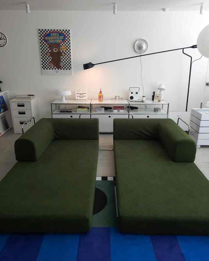 白い壁と棚があるモダンなリビング、中央に配置された緑のソファ２つがあるシンプルな空間