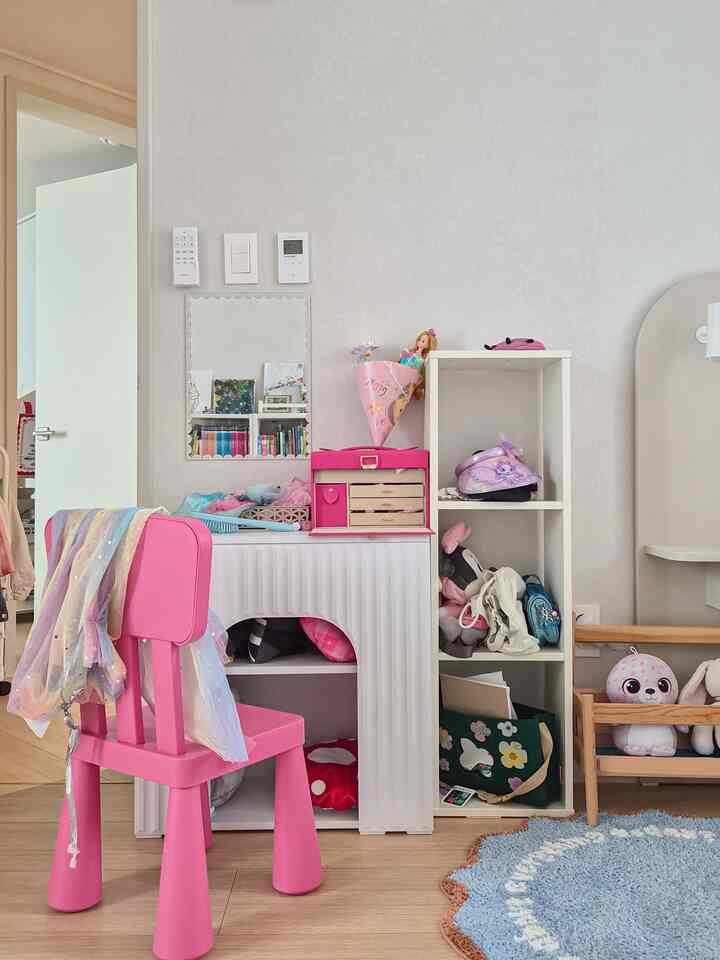 白い壁とピンクの椅子が配置された子供部屋、鏡とミニ化粧台がある清潔感のある可愛らしいインテリア