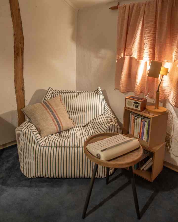 暖かみのあるベージュとブルーのトーンが調和する自然な雰囲気の書斎、ストライプのビーズクッションと木製サイドテーブル、読書用ランプが配置された空間