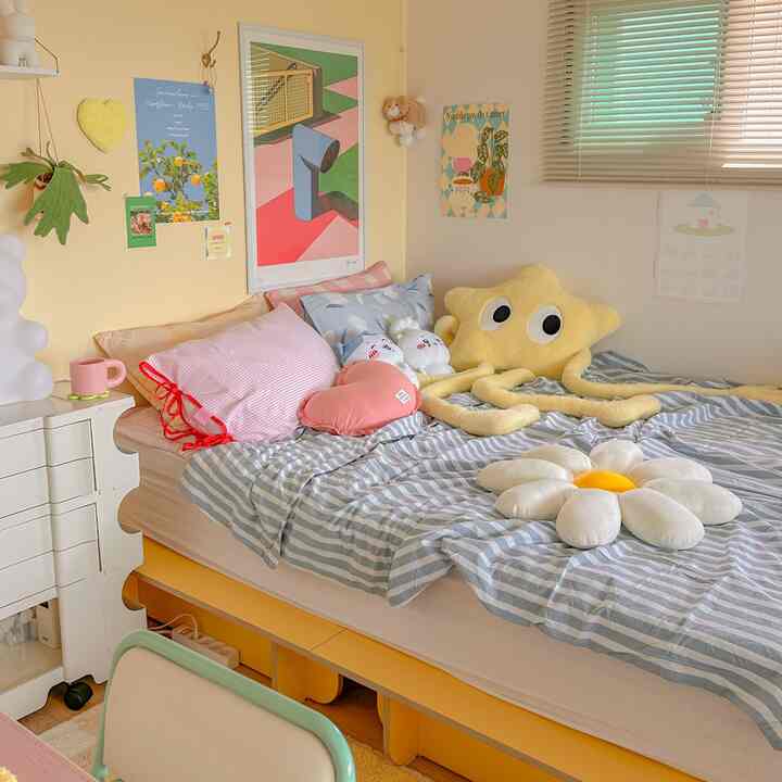 Yellow and white toned kids' room featuring a bed with star and flower-shaped cushions and colorful pillows in a cozy bedroom space