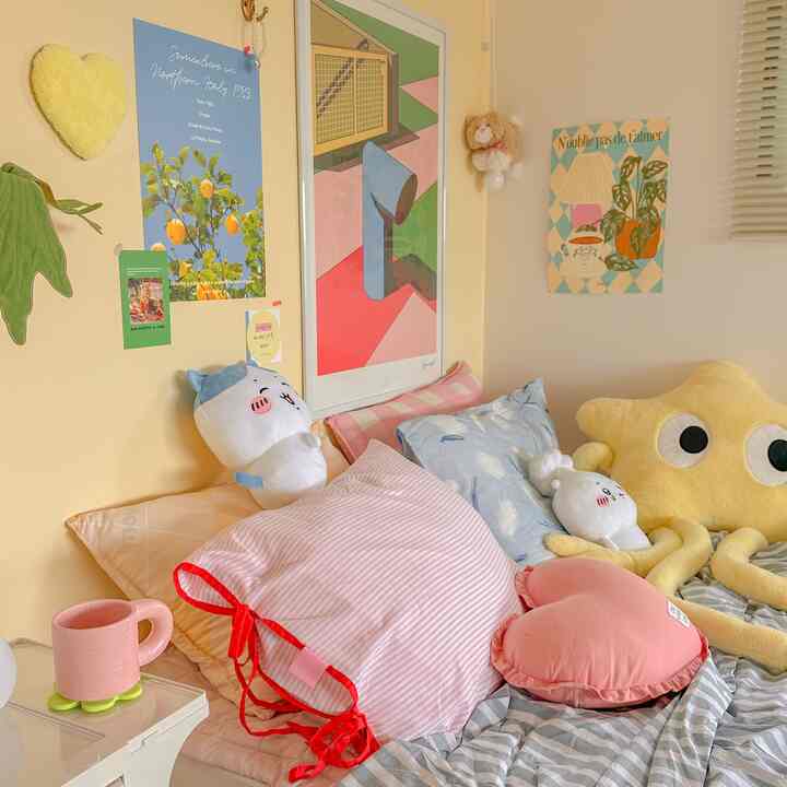 A cozy kids' bedroom in yellow and pink tones, featuring multiple cushions and plush toys arranged on the bed