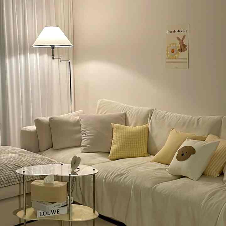 白と黄色のトーンのリビング、広いソファとクッション、フロアランプが配置されたシンプルで暖かな雰囲気のインテリア