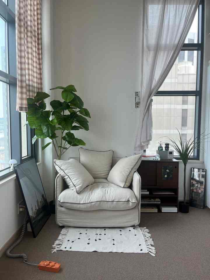 Bright white and green plant-filled studio apartment space featuring a single armchair with a natural and modern vibe