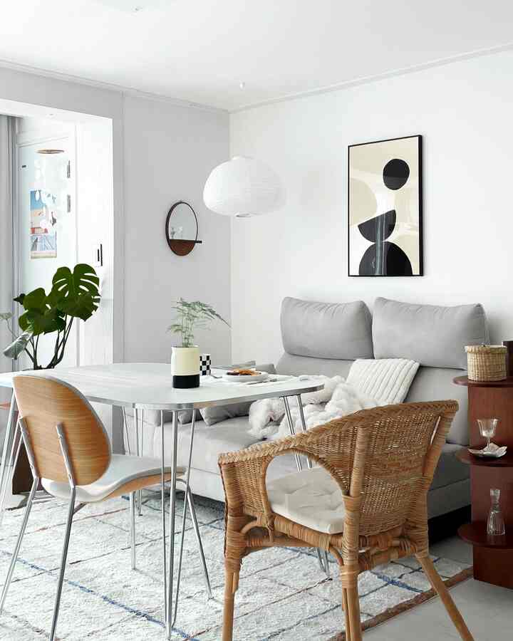 White and silver toned living room featuring a mid-century modern silver-frame dining table with wooden chairs in a clean space