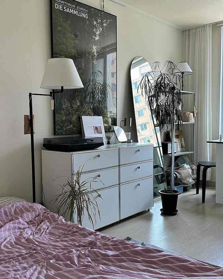 白を基調とした寝室、収納棚が中央に配置され、全身鏡とフロアランプが調和したシンプルなインテリア