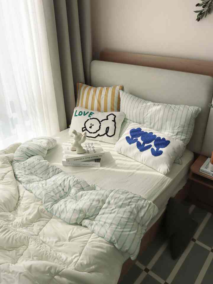 Bright white and natural wood toned cozy bedroom with fabric bed and assorted cushions in a kids' room setting