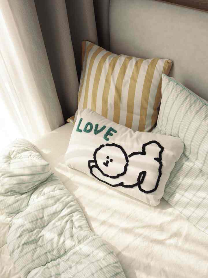 白とナチュラルカラーの子供部屋、ファブリックベッドと刺繍クッションが配置された居心地の良いインテリア