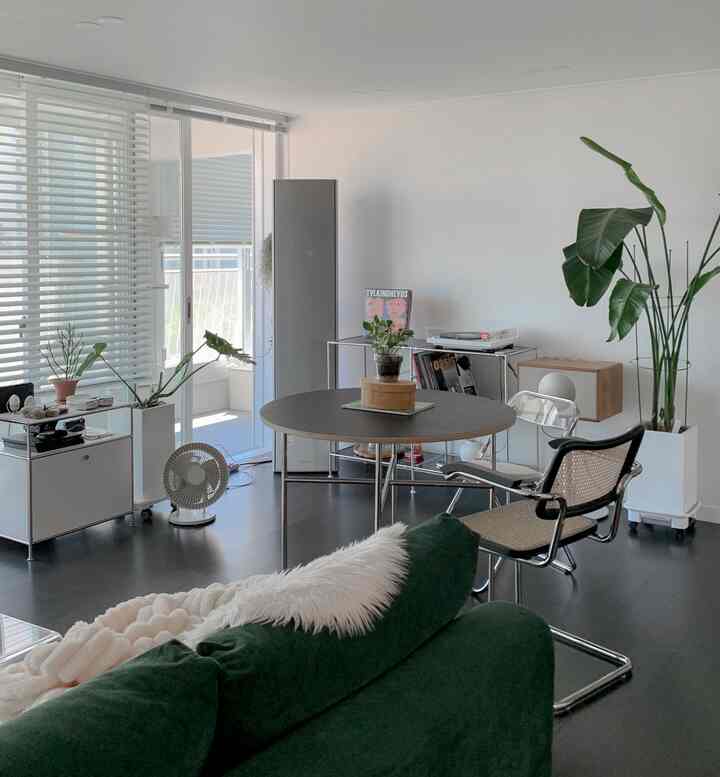 Modern living room with white walls and blinds, green sofa and dining table arranged in the space