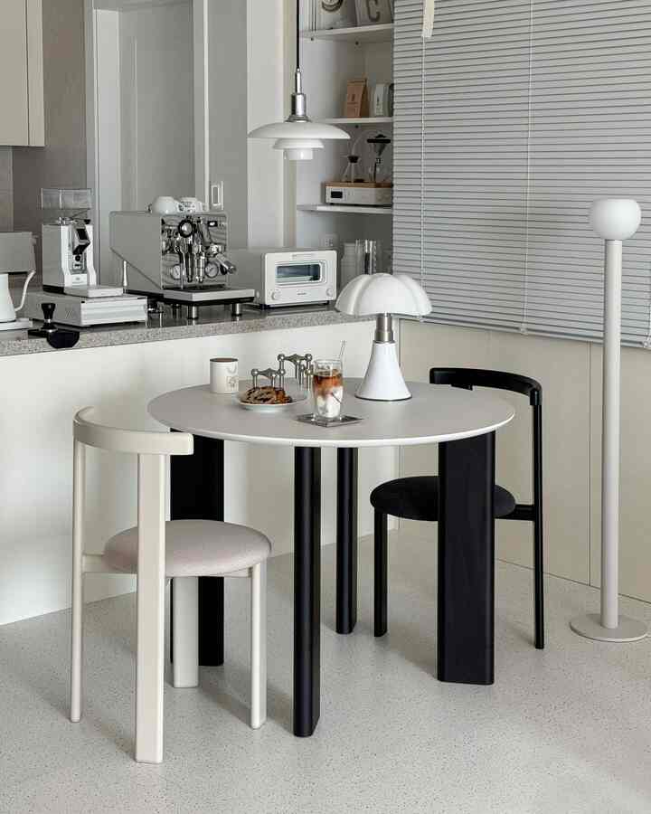 ホワイトとブラックが調和するモダンなキッチンスペース、アーティックテーブルとチェア、コーヒーマシンが配置された清潔感のあるおうちカフェ