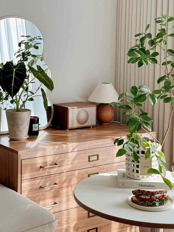 温かみのあるウッドトーンとナチュラルカラーのリビング、木製収納キャビネットと豊富な植物が調和したミニマルなインテリア空間