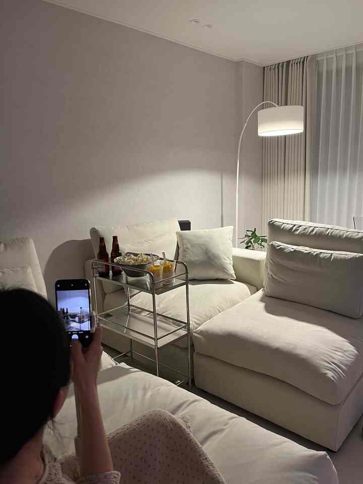 明るいホワイトトーンのリビング、大型ソファとアレックスアークフロアランプ、ステンレス製トロリーが配置された落ち着いた現代的な空間
