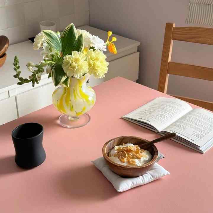 ピンクのテーブルに木目調のダイニングテーブル、花瓶とヨーグルトボウルが置かれた雰囲気のあるキッチンおうちカフェ