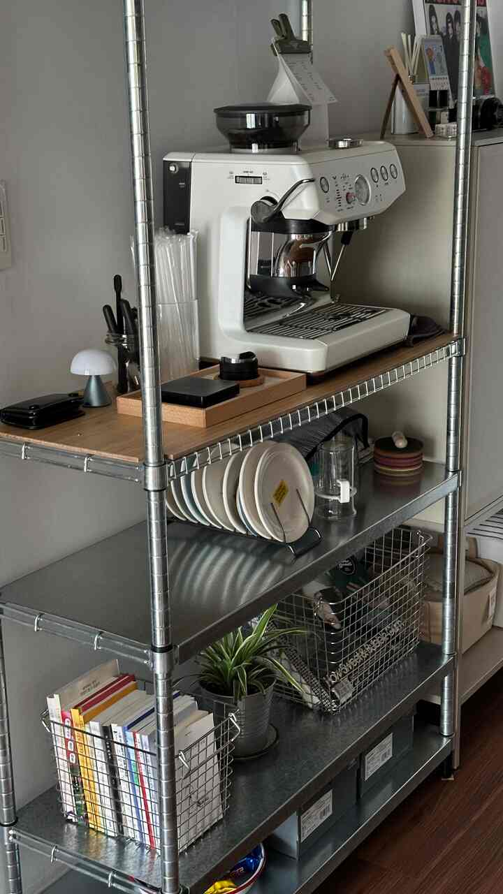 ベージュとスチールのトーンが調和したコンパクトなキッチン空間、イケアの鉄製棚にブレビルのコーヒーマシンや整理されたキッチン用品が配置された雰囲気のあるホームカフェコーナー